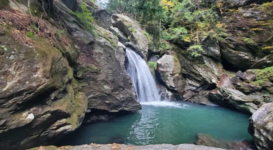 A serene waterfall cascades into a clear, turquoise pool, surrounded by moss-covered rocks and lush greenery, creating a peaceful, natural setting.