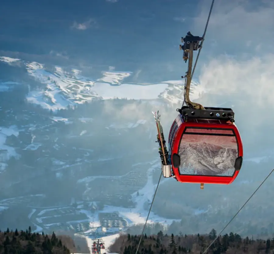 A red ski gondola with ski gear descends over a snowy mountain landscape, conveying adventure and thrill, against a backdrop of cloudy skies.